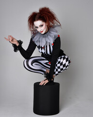 Full length  portrait of red haired  girl wearing a black and white clown jester costume,...