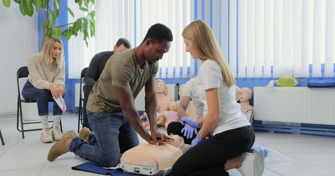 Young woman instructor showing how to make chest compressions with dummy during the first aid group training indoors.