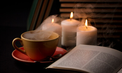 Obraz na płótnie Canvas cup of coffee with smoke and candles alfon with books (focus on cup)