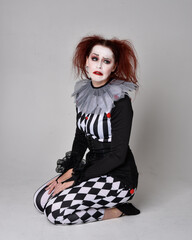Full length  portrait of red haired  girl wearing a black and white clown jester costume,...