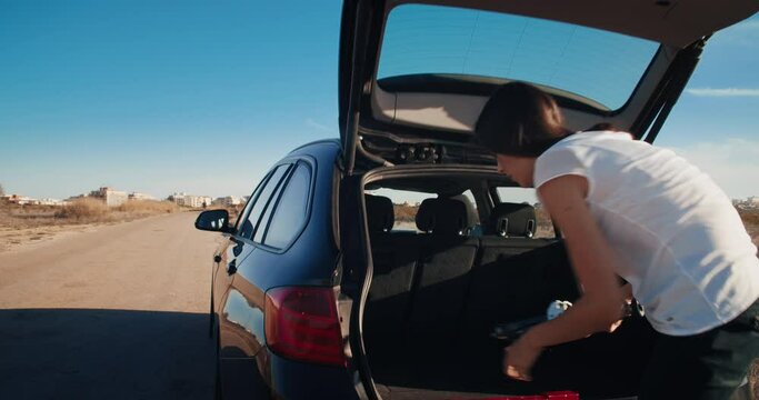 Young woman takes jack out of the trunk and going lift the vehicle. Attractive woman has tire flat car breakdown during travel on country road 