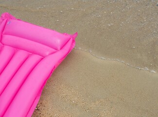 Pink bed mattress float laying on the sand on the beach. With space for place your text.