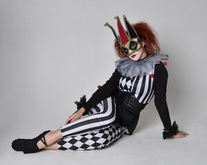 Full length  portrait of red haired  girl wearing a black and white clown jester costume,...