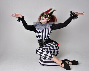 Full length  portrait of red haired  girl wearing a black and white clown jester costume,...