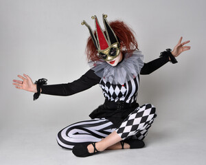 Full length  portrait of red haired  girl wearing a black and white clown jester costume,...