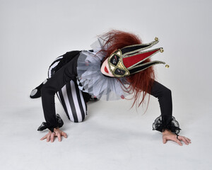 Full length  portrait of red haired  girl wearing a black and white clown jester costume,...