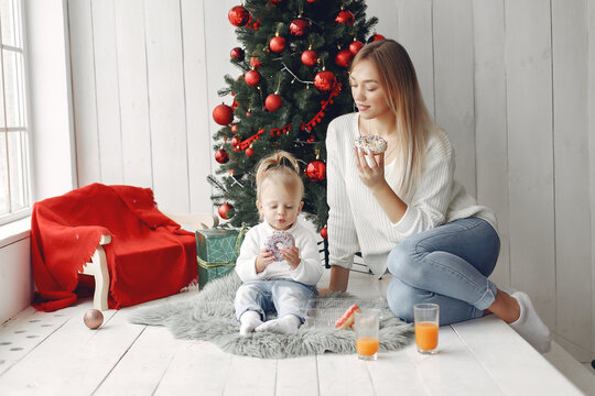 Mother with little daughter sitting near Christmas tree and and go donuts.