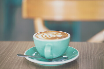 Hot latte art in green ceramic cup on wooden table with art texture