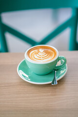 Hot latte art in green ceramic cup on wooden table with art texture