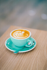 Hot latte art in green ceramic cup on wooden table with art texture