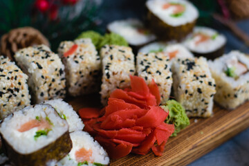 Large sushi set on a wooden board. Rolls with sesame seeds, nori, cheese, red fish, cucumber and eel, ginger, wasabi and christmas decor on gray background