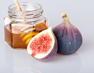 Fresh delicious young whole figs and half a ripe beautiful fig. A jar of honey with a honey spoon in the background, isolated on a white background