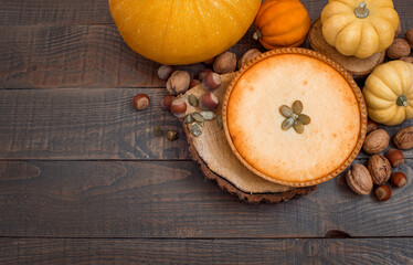 Fototapeta premium Pumpkin pie on wooden stands surrounded by pumpkins, walnuts and chestnuts on a dark background.