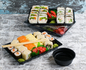 Several sets of sushi with wasabi and soy sauce in plastic packaging on a light gray background. Delicious rolls with shrimp, cucumber and spinach. Food delivery to your home or office.