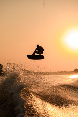 silhouette of active man making trick with wakeboard on bright orange sky and sun background.