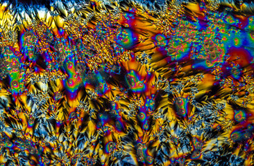 Extreme macro photograph of Vitamin C crystals forming abstract modern art patterns, when illuminated with polarized light, under a microscope objective with 10x magnification