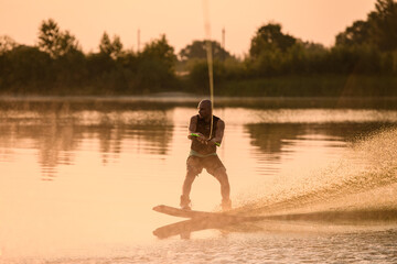 adult sporty man holds the handle of cable and balances with a wakeboard on the water