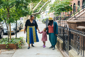 Naklejka premium Lesbian parents walking down city street holding hands with their daughter