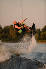 active strong man holds rope and making extreme jump showing trick with wakeboard.
