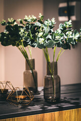 Eucalyptus branches in a vase are on a shelf. Nearby is a bronze metal candlestick.