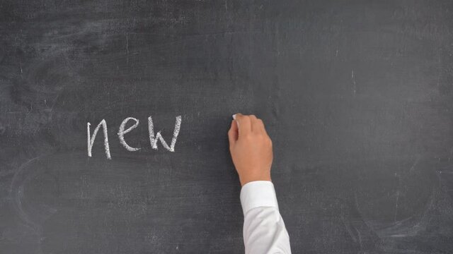 A man's hand writes the phrase NEW SKILLS on a chalkboard