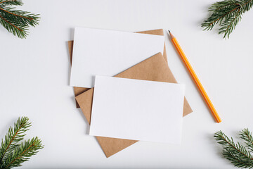 Christmas greeting cards mock-up for invitations or xmas wishes, flat lay. Top view of pine sprigs, craft envelopes, pencil and two white cards with empty space. Happy new year festive layout