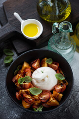 Burrata cheese with cherry tomatoes and fresh green basil served in a black bowl, elevated view, vertical shot