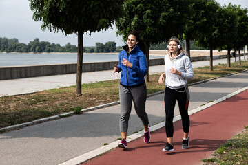 Two young woman friends and business partners owners of small company practicing morning routine by running outdoor before they go to the office. Sporty females exercising jog and run outside. 
