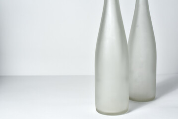 two empty wine bottles without labels standing on a table against a white background