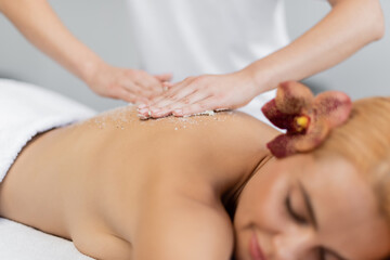 Obraz na płótnie Canvas professional masseur applying body scrub on back of blurred client