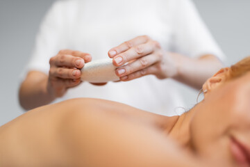 cropped view of blurred masseur placing hot stone on body of client in spa center
