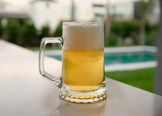 Summer vibes. Closeup view of cold beer mug on the table. The foam, golden liquid and glass on the table in the garden at sunset.