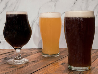 Brew. Closeup view of three glasses with different kinds of beers, black, red and golden, on the pub wooden table with a white marble background.