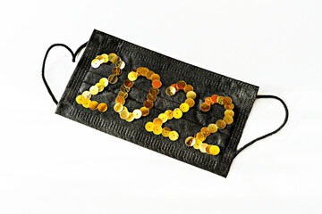 Black medical face protective mask with new year 2022 numbers made of golden sequins on a white background close-up , Healthy New Year concept