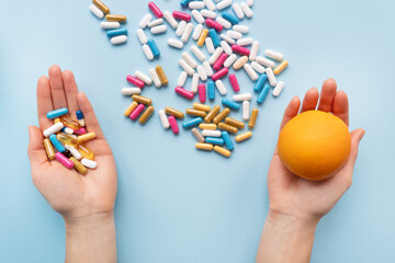Many multi-colored pills, man's hands in one vitamins in another fresh orange. Health and treatment alternatives concept.