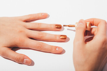 Woman hands doing manicure with shiny bronze nail polish