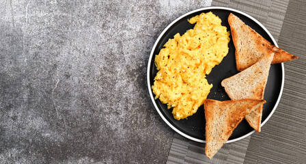 Scrambled eggs with toast on a round plate on a dark background. Top view, flat lay