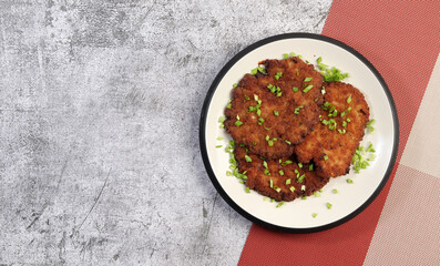 Traditional Fried Wiener Schnitzel on a round plate on a dark gray background. Top view, flat lay