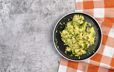 Scrambled eggs and scallions on a round plate on a dark gray background. Top view, flat lay