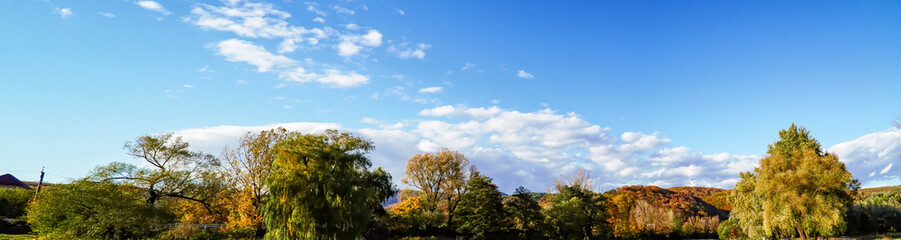 Obraz premium panorama of trees, white clouds over the mountains, early autumn, blue sky 
