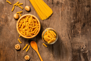 Pasta; a wooden bowl and jar of fusilli and spaghetti, with a bowl of button mushrooms, a bowl of cherry tomatoes and plate of garlic