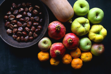 Pan with chestnuts, butternut squash and various fruit on dark background. Flat lay.