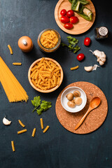 Obraz na płótnie Canvas Dried fusilli in a wooden bowl with cherry tomatoes, a white bowl of button mushrooms and garlic on a navy blue background