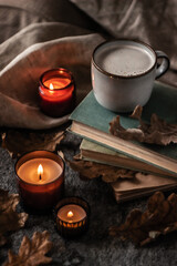 old books, coffee cup and burning candles with dry oak leaves on a stone background