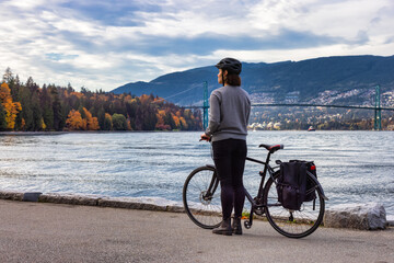 White Caucasian Adult Woman riding a bicycle on Seawall in Stanley Park. Cloudy Fall Season....