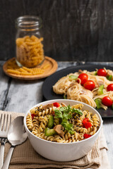 A bowl of fusilli with green peppers and cherry tomatoes on a white wood table