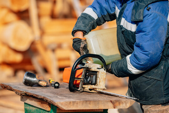 Closeup Lumberjack refueling chainsaw with gasoline building wooden log house