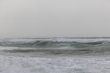 A dramatic view of a very choppy sea with huge crashing waves during a major storm under a grey sky