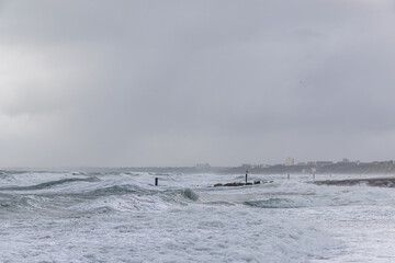 A dramatic view of a very choppy sea with huge crashing waves on groynes (breakwater) during a major storm under a grey sky