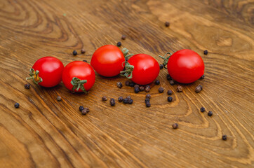 Little red cherry tomatoes on wooden board background Scattered pepper peas